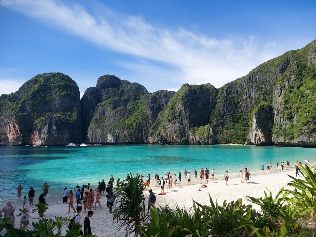 Crowded beach scene at picturesque Maya Bay with stunning cliffs and turquoise water, ideal for travel and leisure imagery.